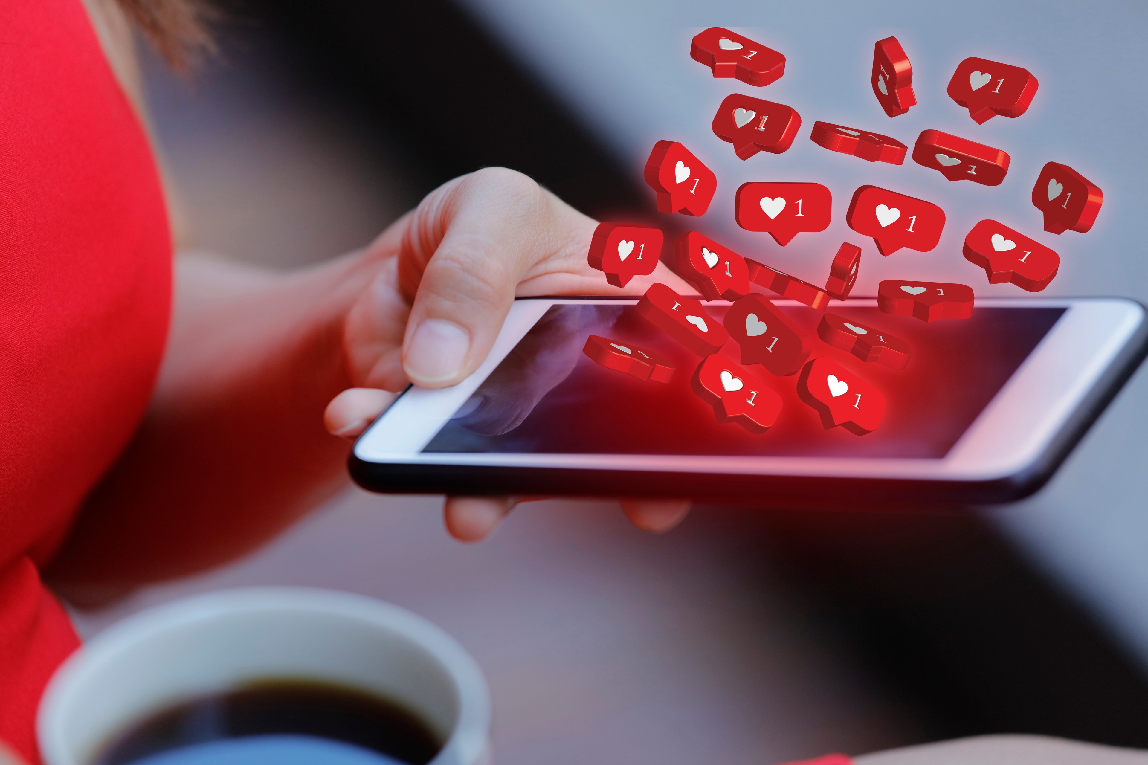 A woman on social media on her phone with hearts representing likes. 