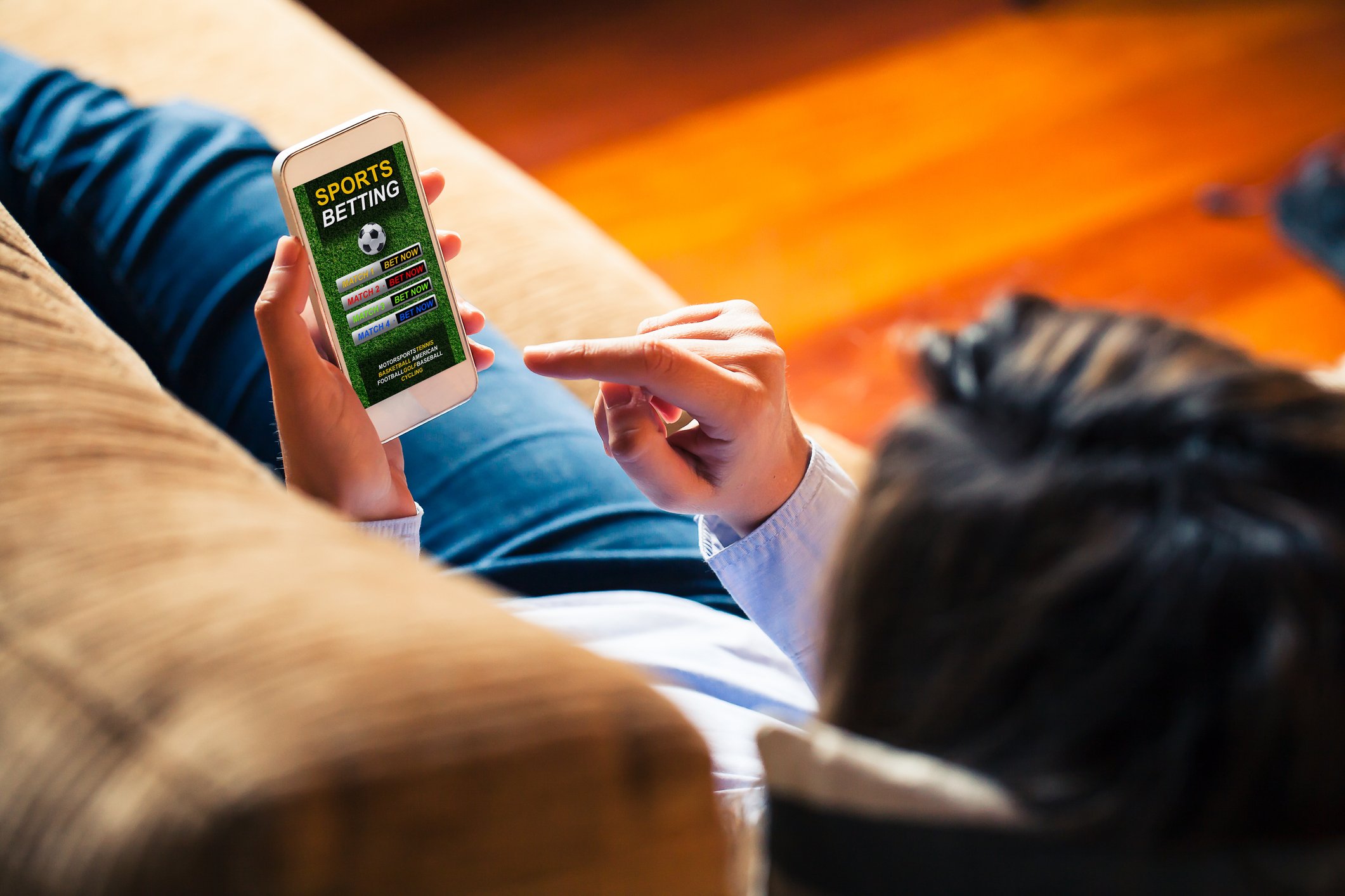online sports gambler on couch with smartphone making bets