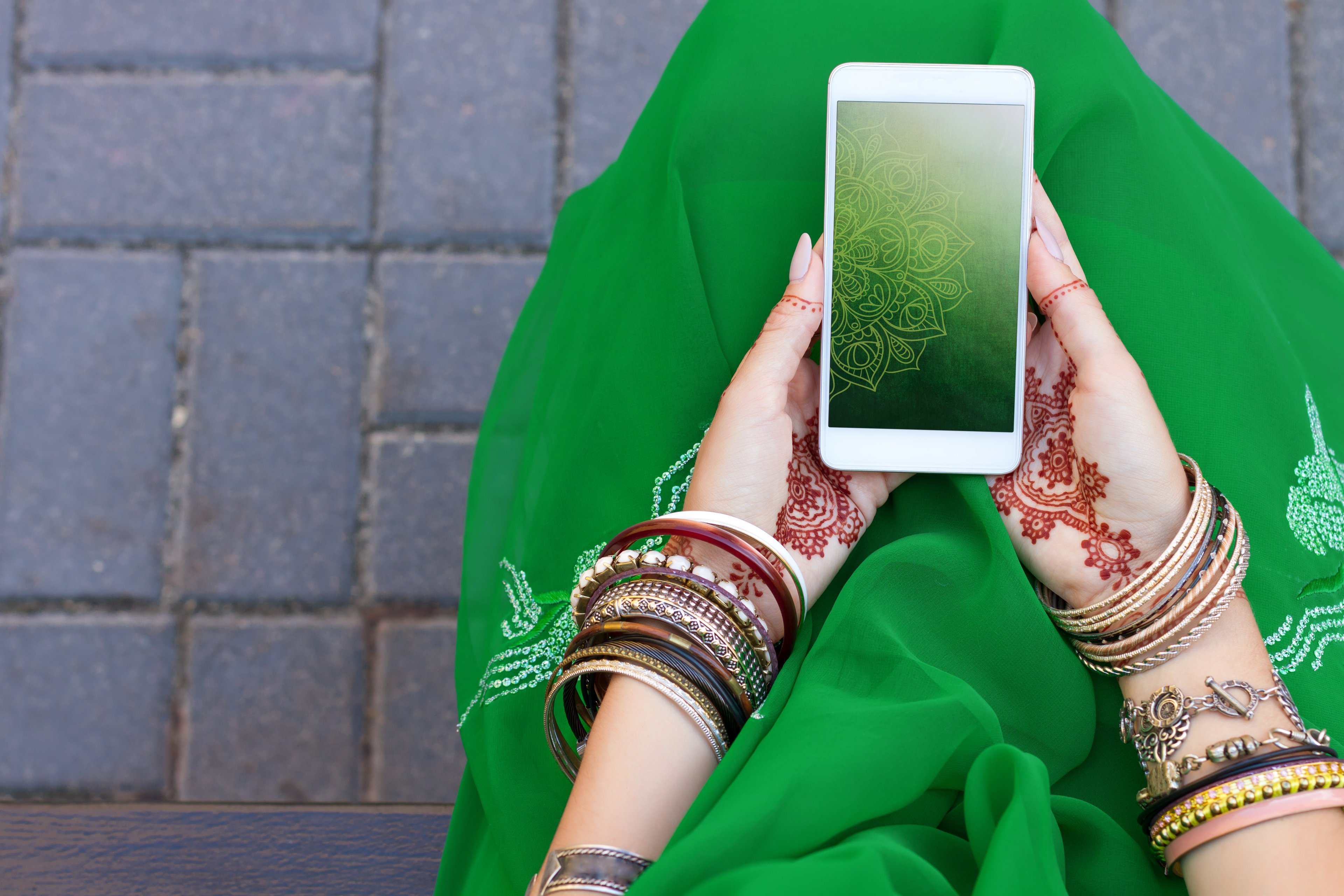 An Indian woman sitting down outside holding a smartphone. 