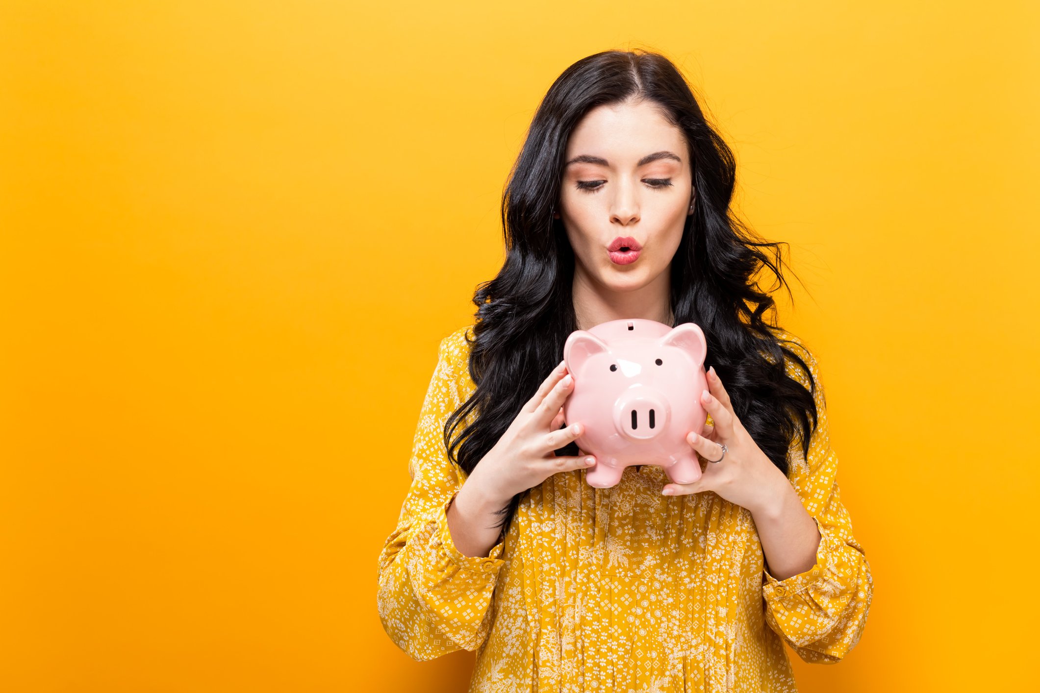 Young woman holding piggy bank against yellow background