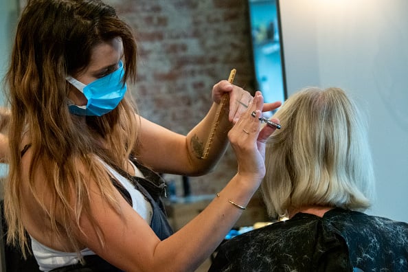 A hairdresser wearing a mask gives a client a haircut.