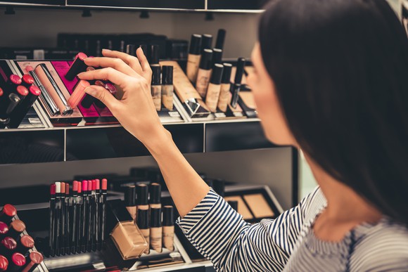 Women touching various cosmetics on a shelf in a store.