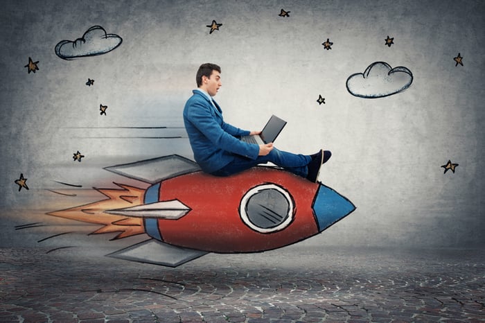 A businessman on a laptop riding a cartoon rocket.