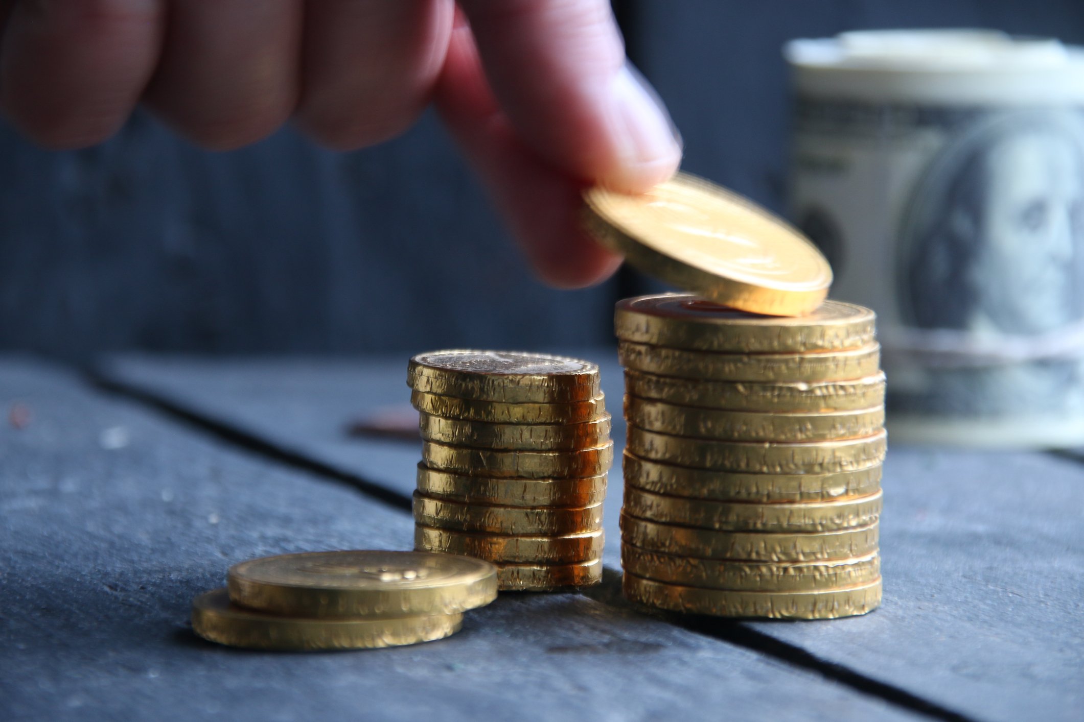 Stacks of gold coins and a person placing a coin on one of the stacks. 