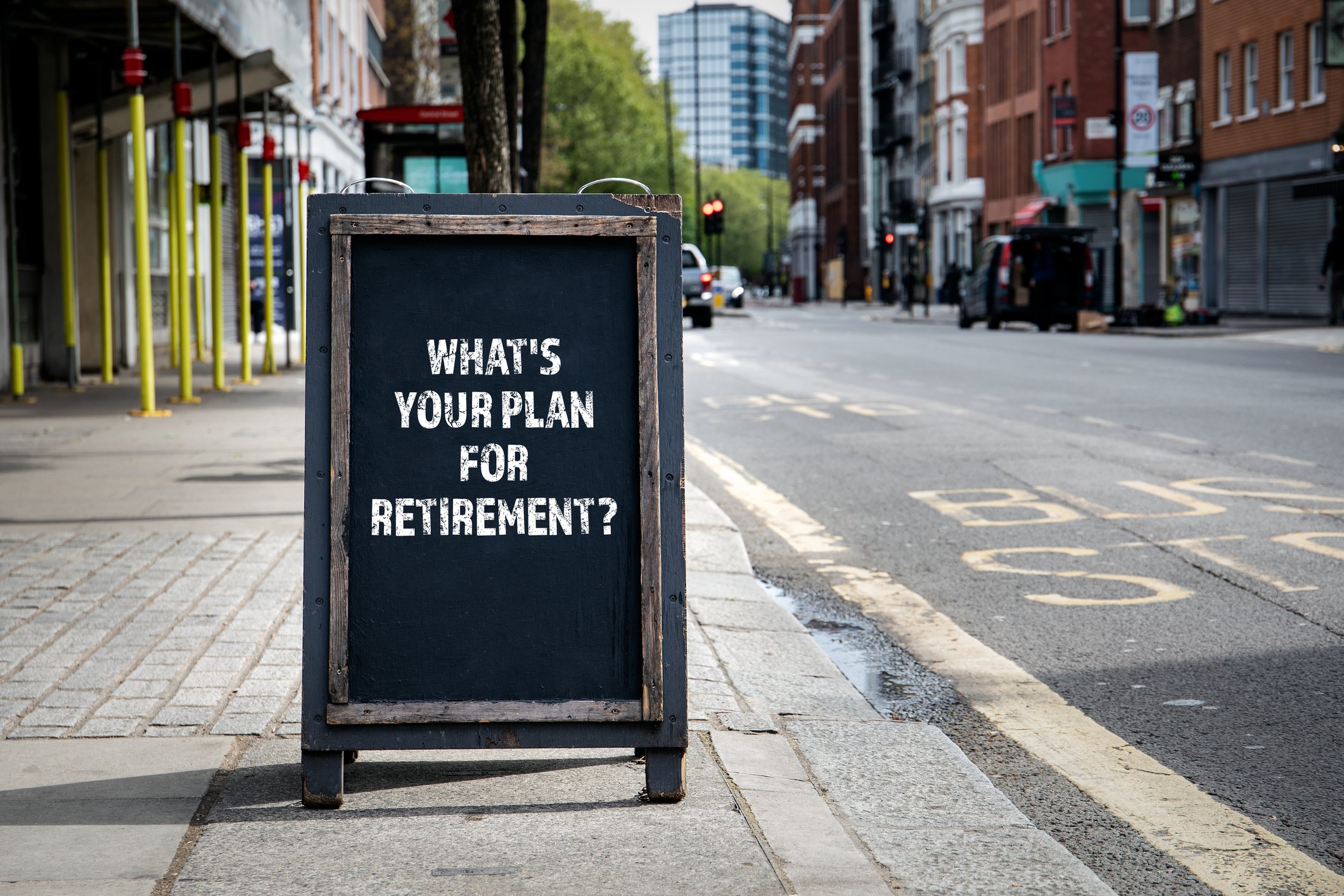 A wooden sign on a sidewalk in a city that says What's Your Plan for Retirement?