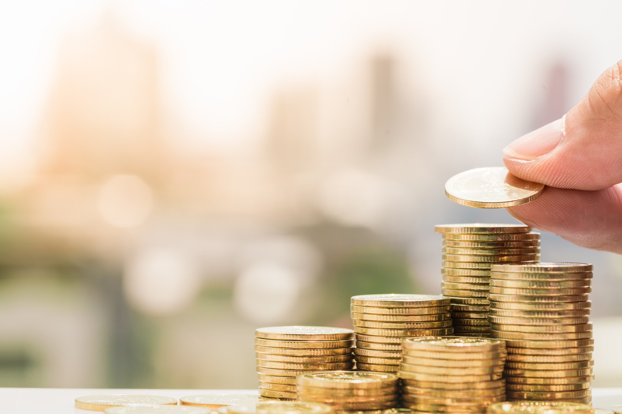 Close-up photo of a hand stacking gold coins in increasingly tall piles.