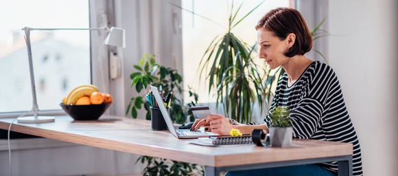 Woman at a table typing on a laptop while holding a credit card.