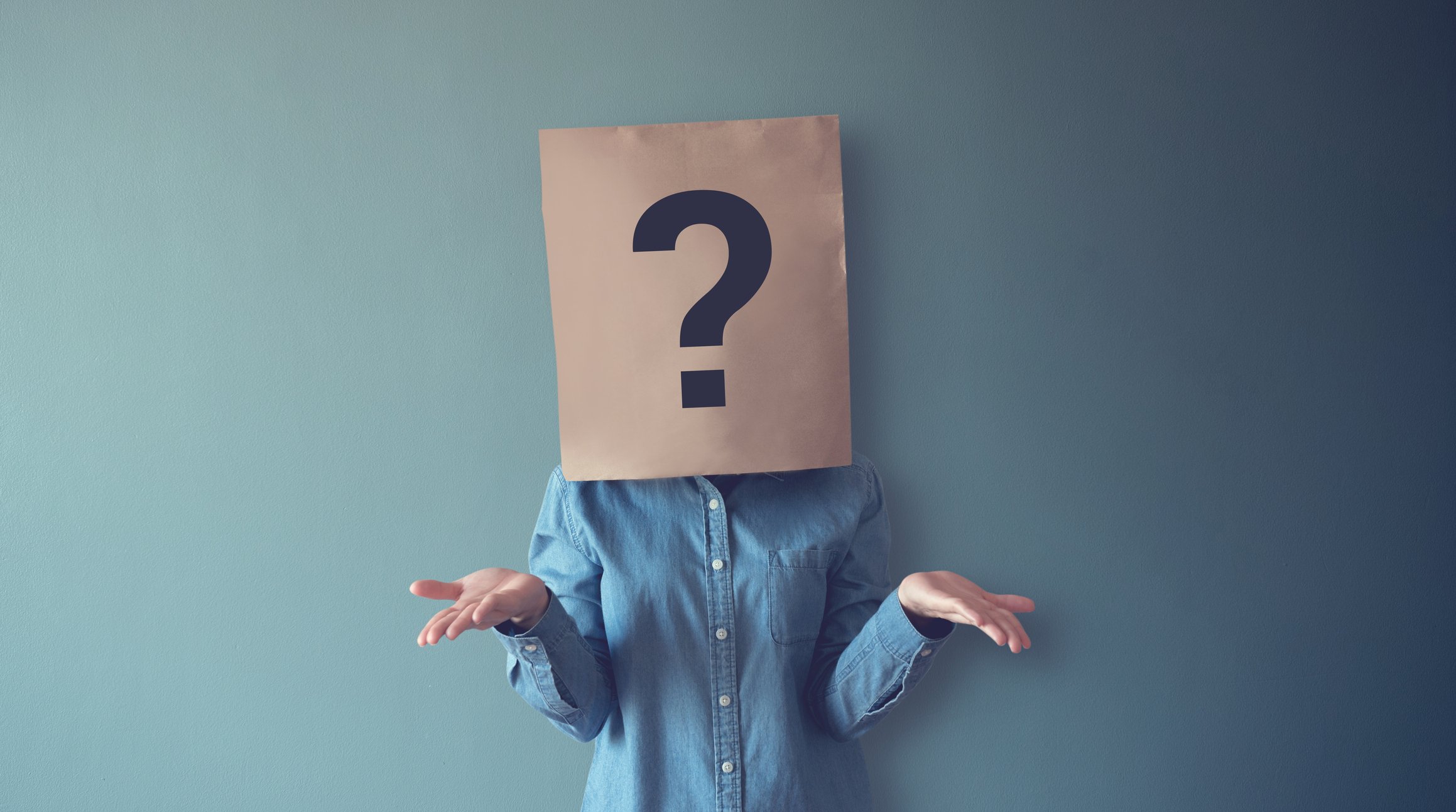 A woman shrugging while a paper bag with a question mark covers her head. 