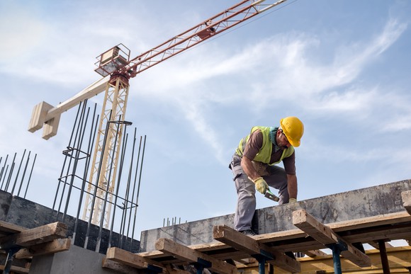 Construction worker handling reinforced concrete with crane in background.