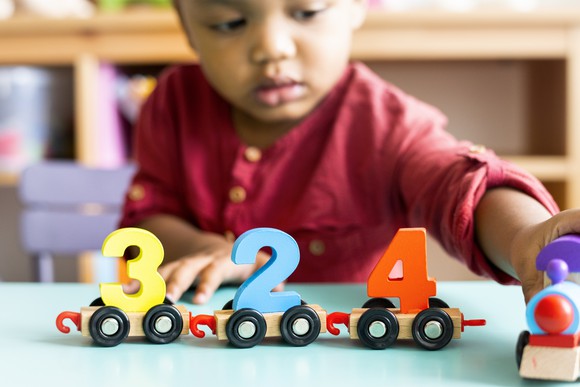 A toddler playing with a number wood toy in a daycare setting. 
