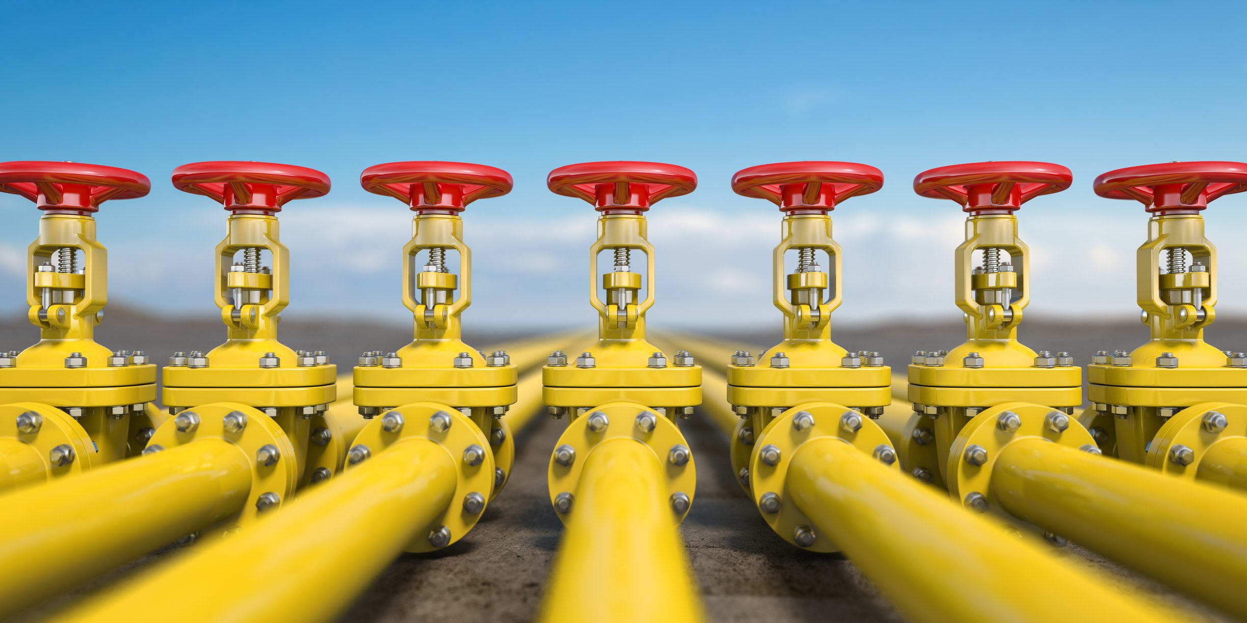 A line  of six yellow oil pipelines with red  handles sticking out on top. 