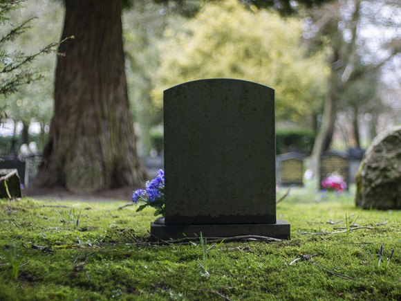 Gravestone with flowers near it, and trees and other graves behind.