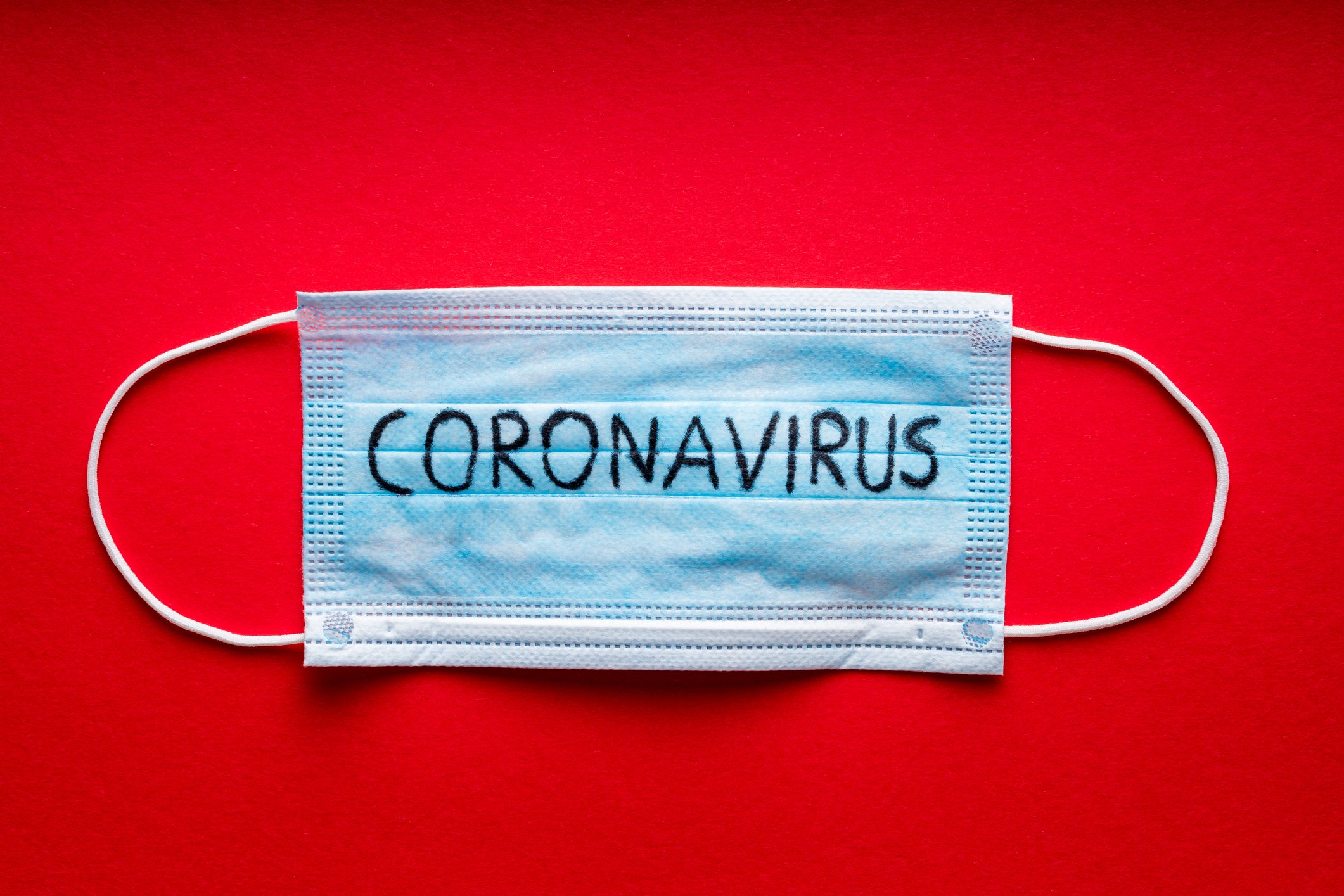 A mask with coronavirus written on it is shown against a red background.