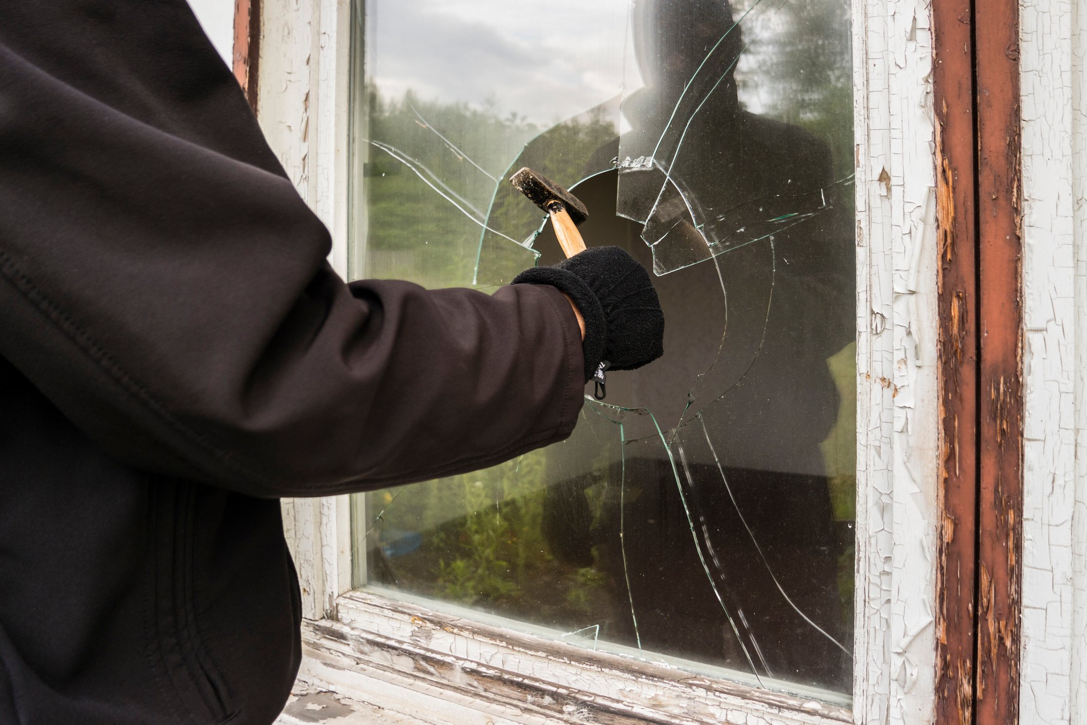 A person in a black jacket breaks a window with a hammer.