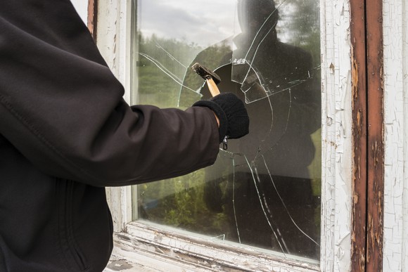 A person in a black jacket breaks a window with a hammer.