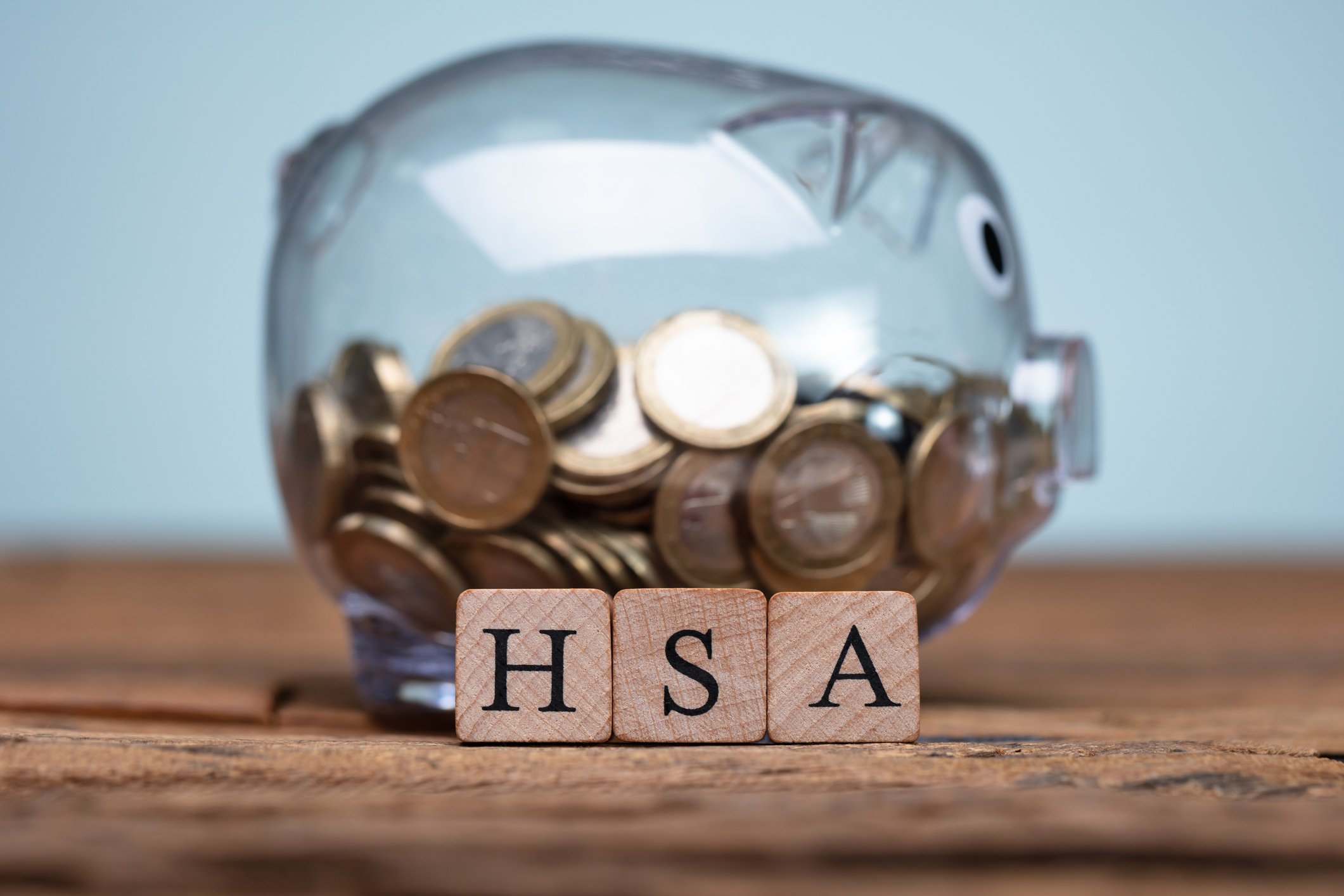 Wood blocks spelling HSA in front of a glass piggy bank with coins in it