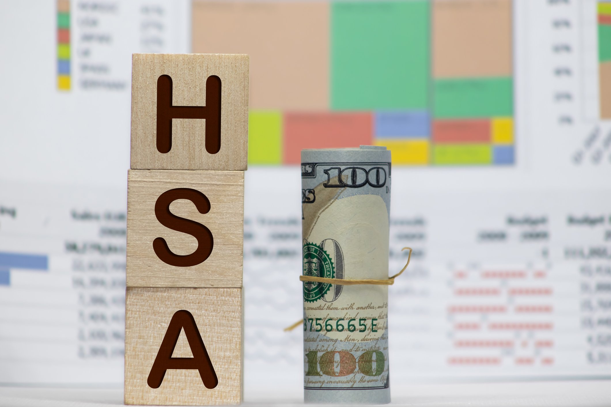 Blocks spelling HSA next to a $100 bill rolled up