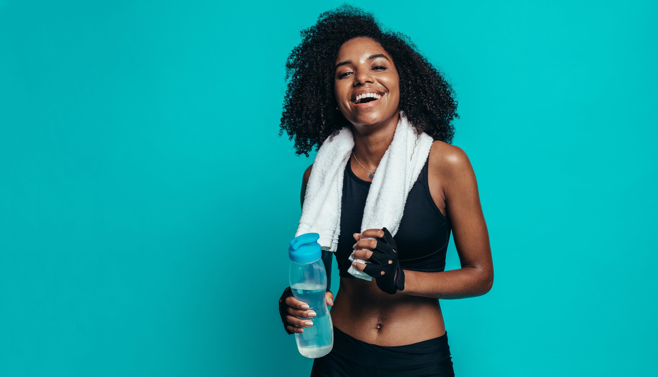 A young woman, with a towel around her neck, smiling and holding a water bottle.