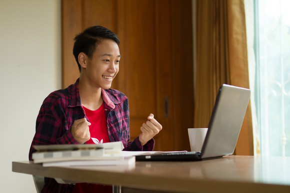 A young student celebrates in front of a laptop.