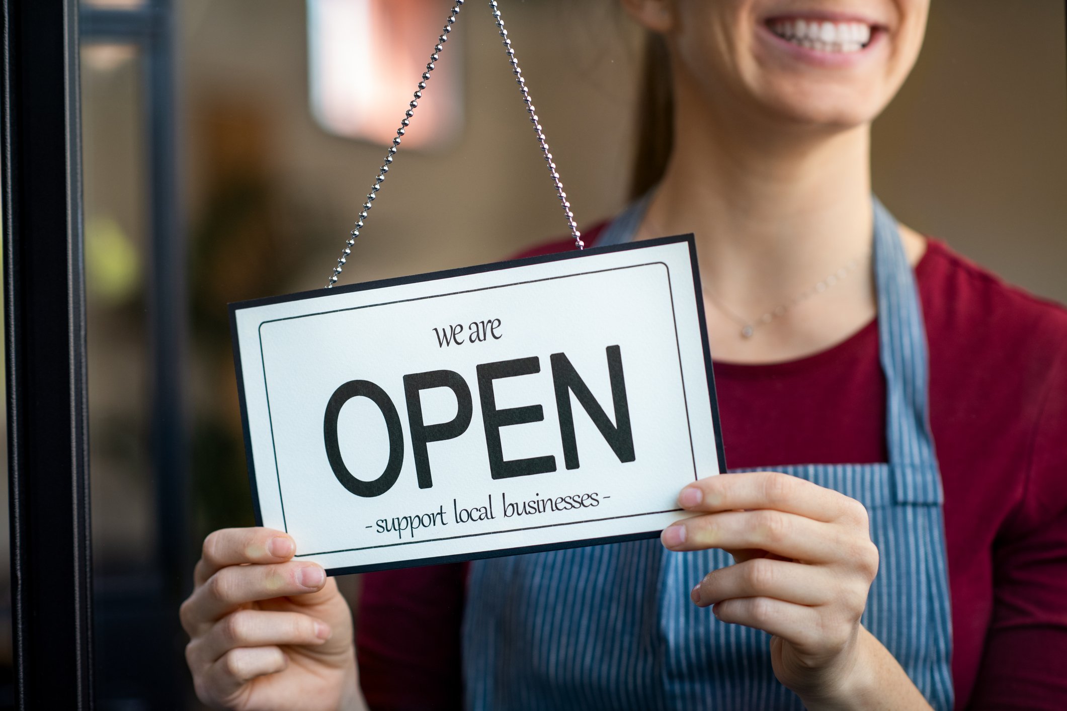 Woman holding open sign in storefront window.