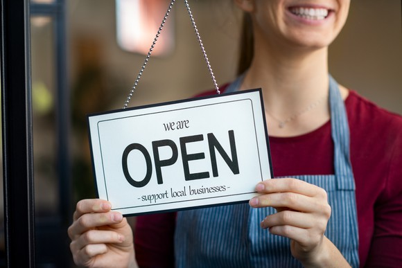 Woman holding open sign in storefront window.