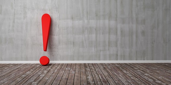 A red exclamation point sits on a wood floor leaning against a wall.