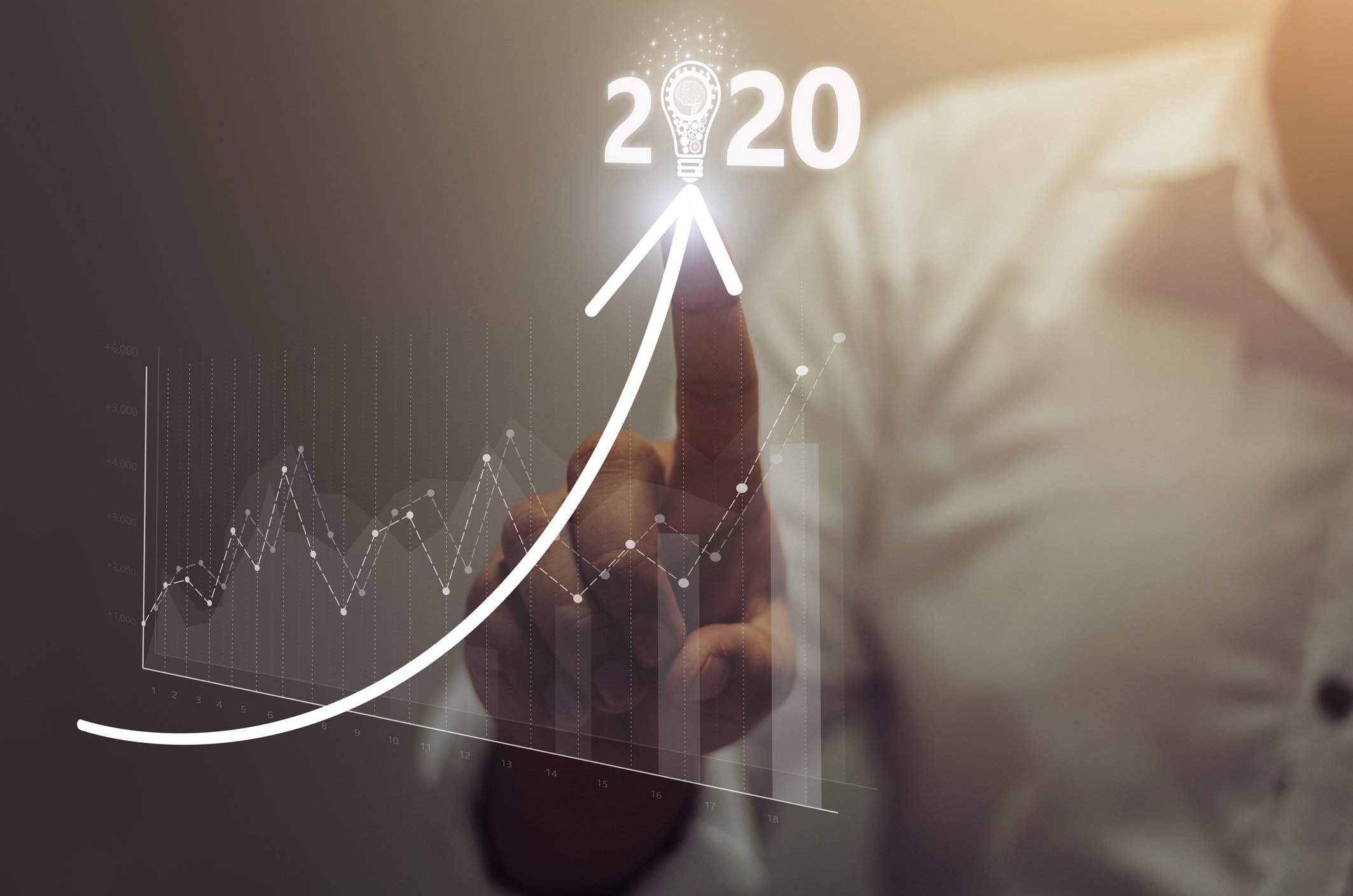 A businessman drawing a positive trending curve with his index finger. 2020 sits at the apex of the curve.