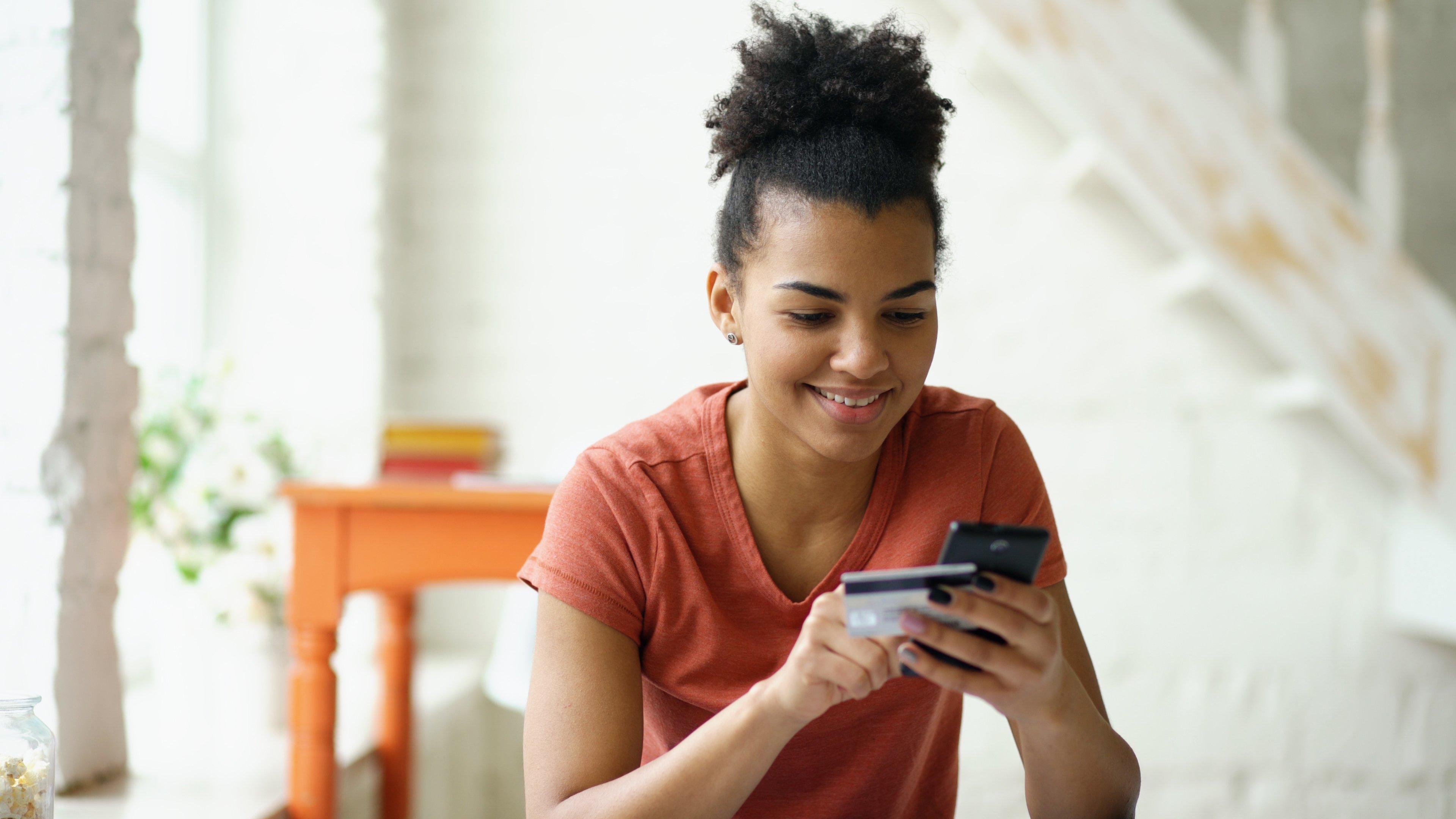 A woman holds her phone and credit card as she places an online shopping order.