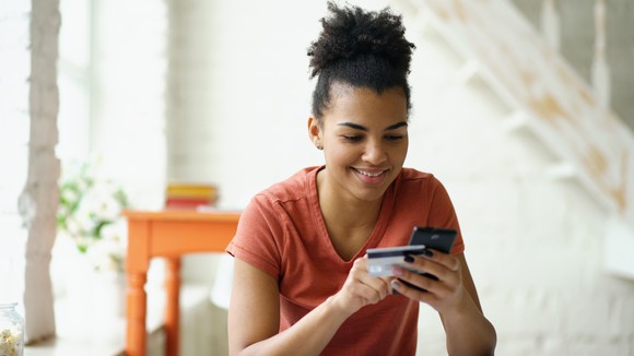A woman holds her phone and credit card as she places an online shopping order.
