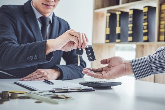 Man in a suit handing  a rental-vehicle key to a customer
