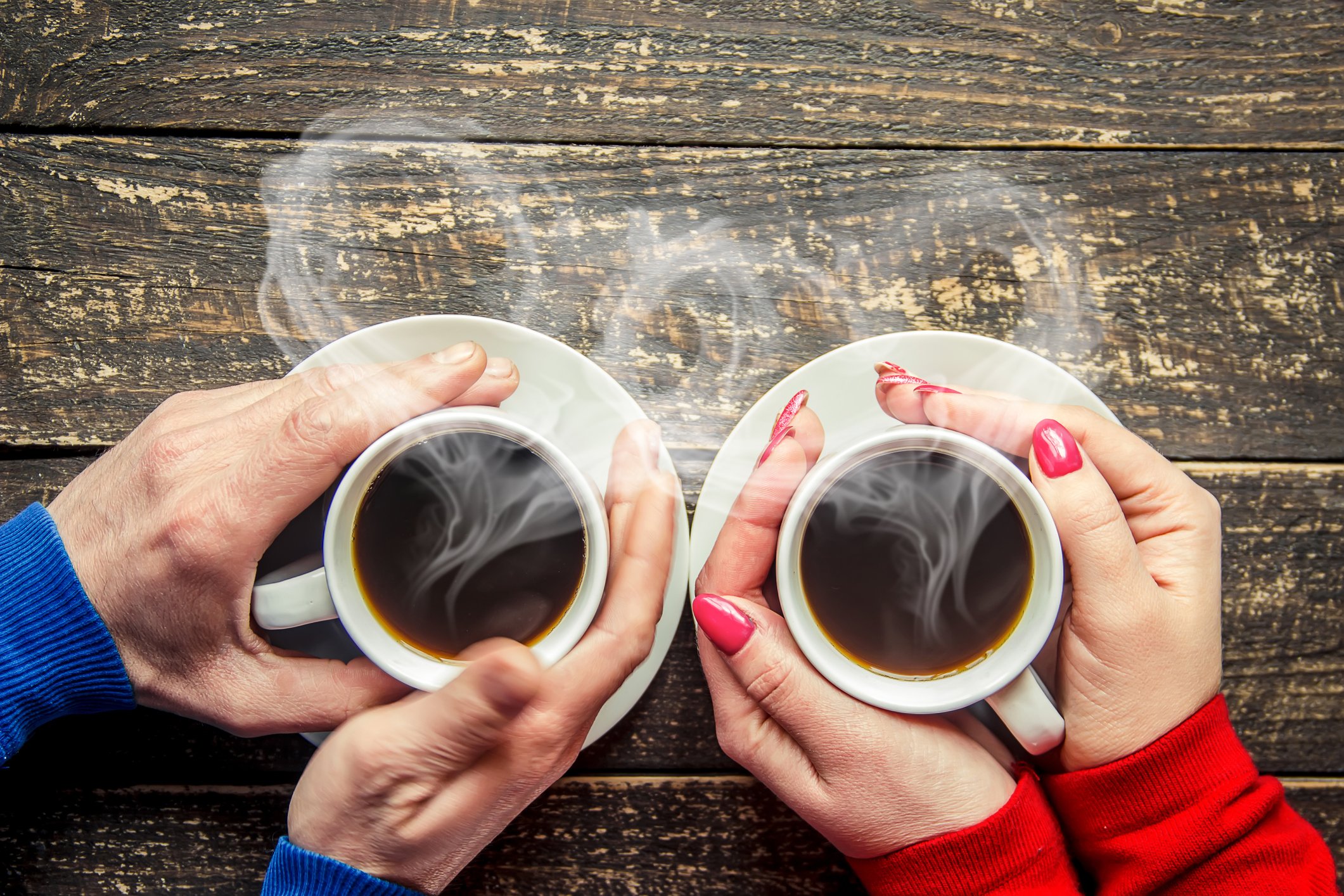 Two pairs of hands wrapped around steaming cups of coffee.