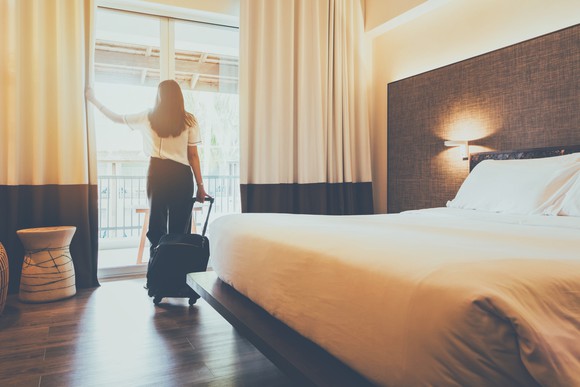 Woman holding luggage standing near sliding door in hotel room