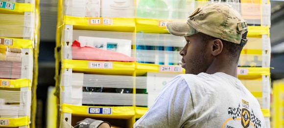 An Amazon warehouse employee loads an item onto a shelf.