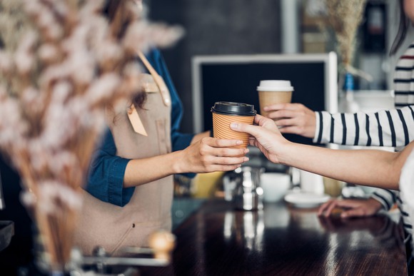 Several arms reaching across counter with coffee cups.