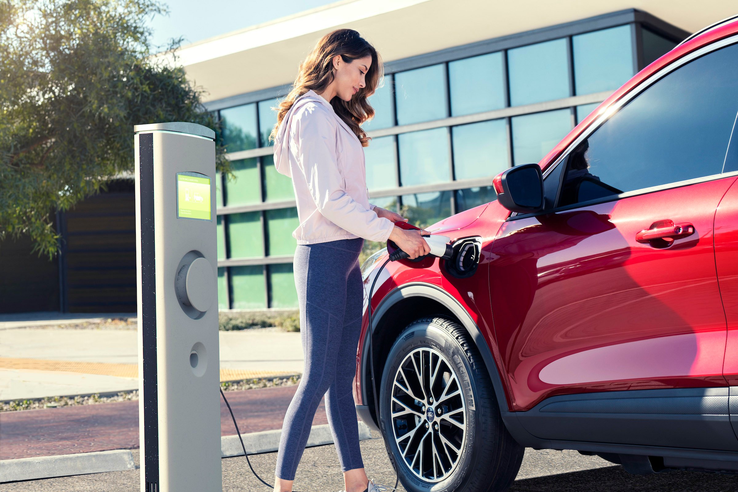 A woman plugs a charger into a red Ford Escape plug-in hybrid SUV.