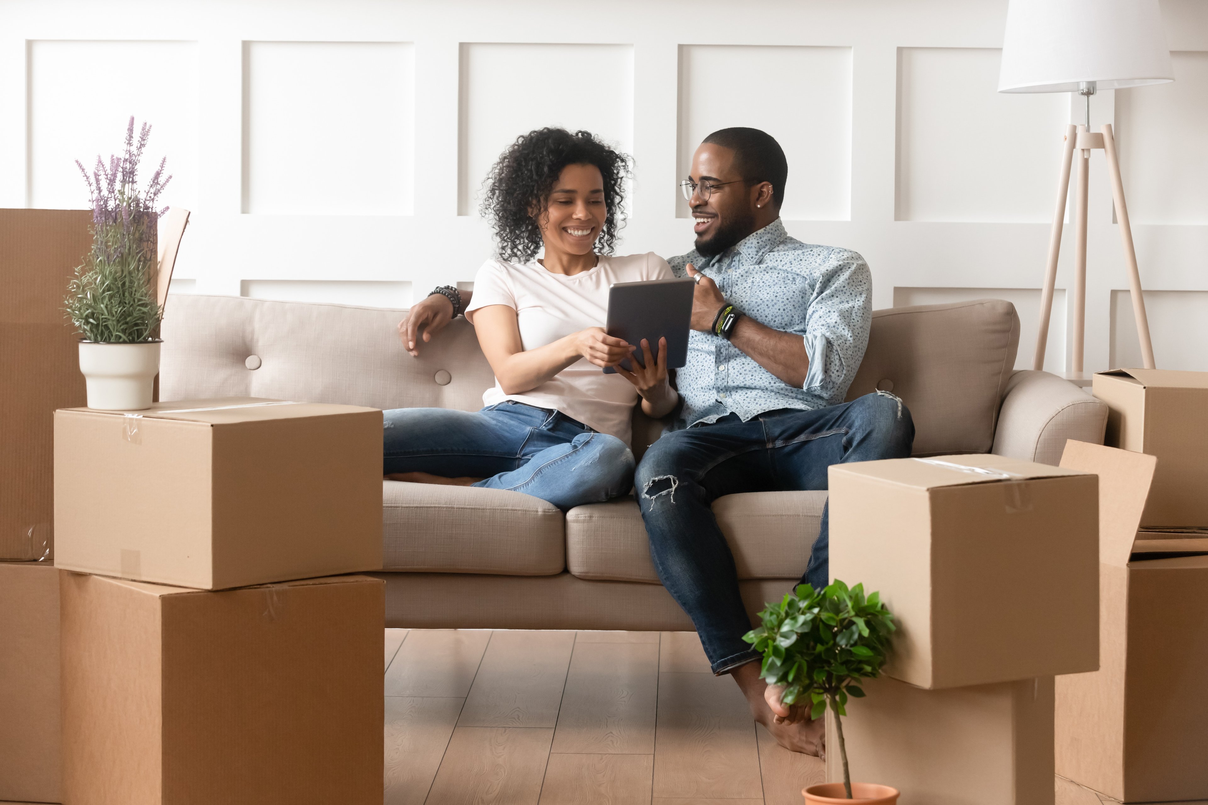 A couple sitting on a couch looking at real estate online with boxes around them.