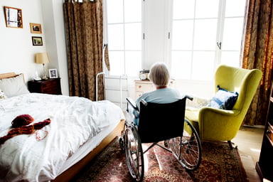 Woman in wheelchair facing window in bedroom
