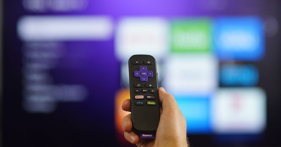 A person's hand holding a Roku remote.