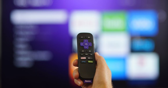 A person's hand holding a Roku remote.