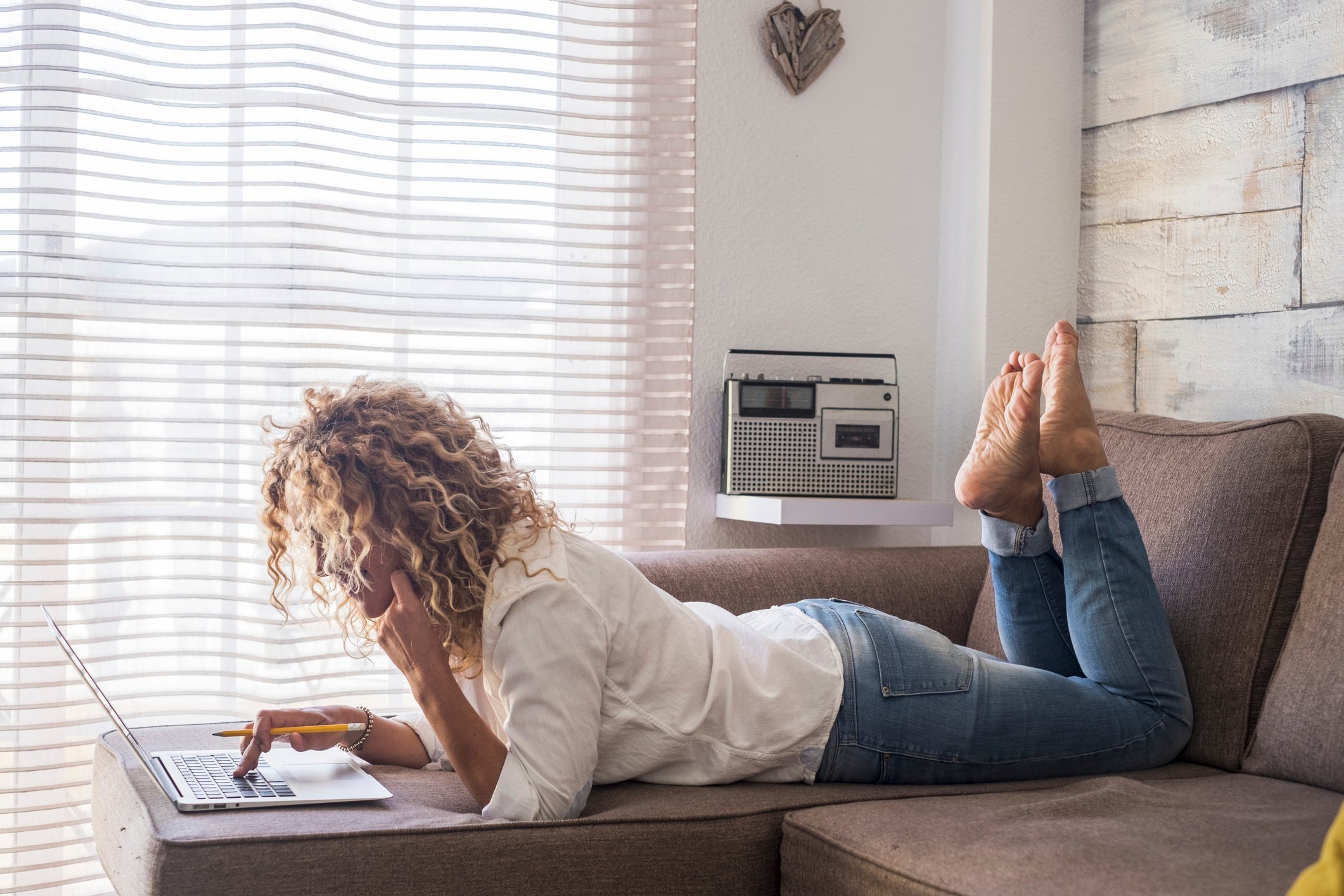 Woman lying on her sofa while using her laptop. 