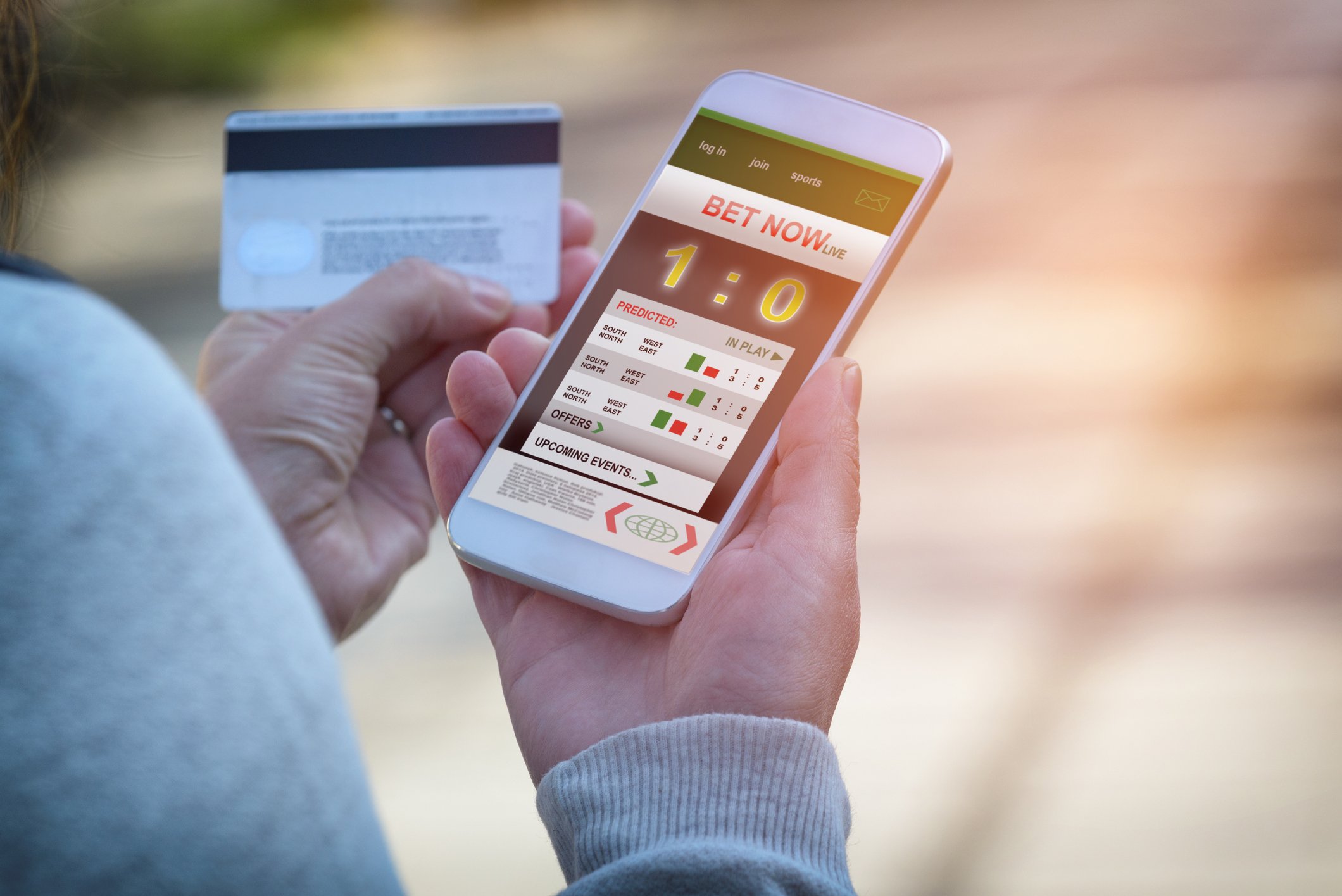 With a credit card in hand, a bettor uses a betting app on a cellphone.