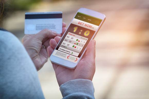 With a credit card in hand, a bettor uses a betting app on a cellphone.