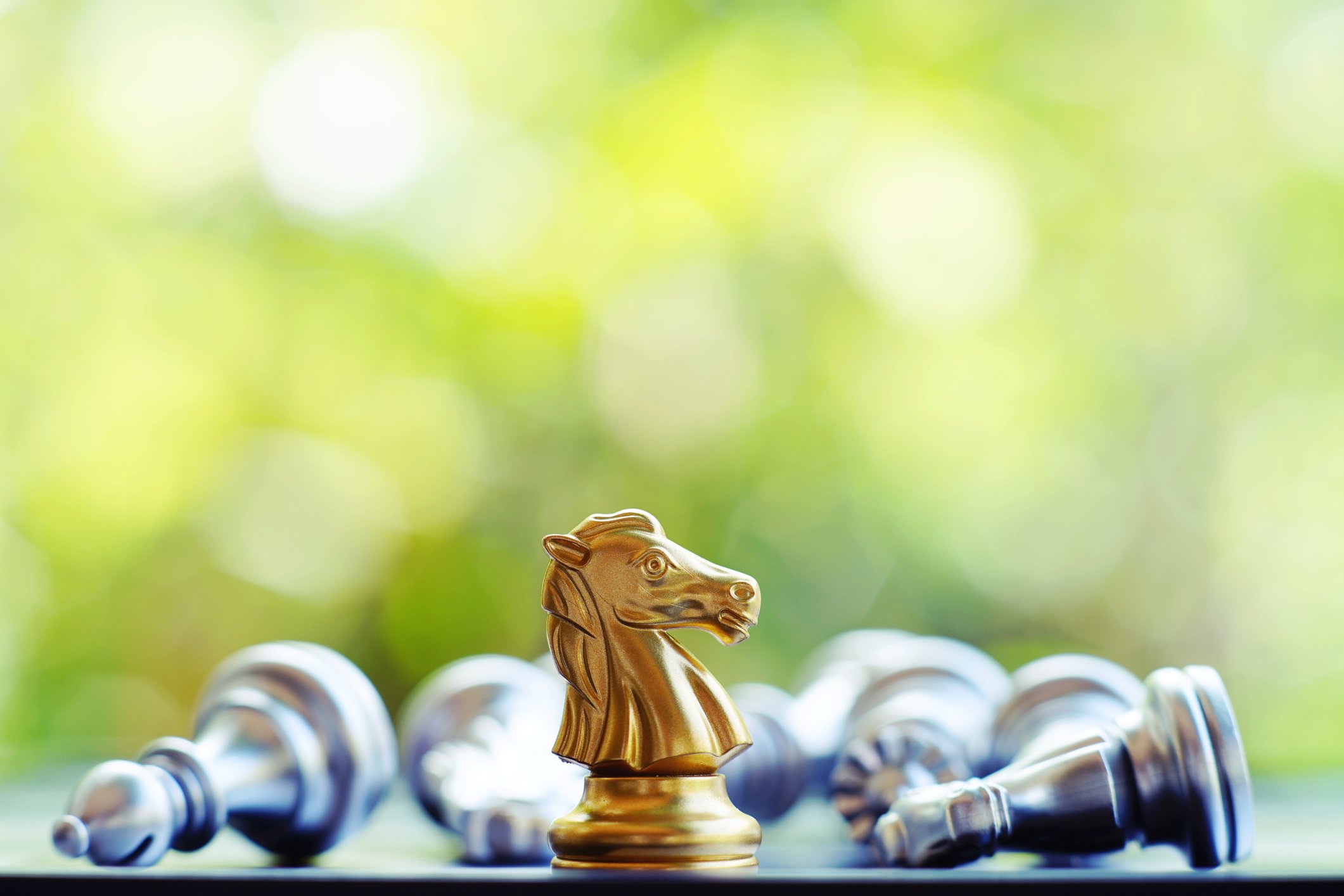 A golden chess knight stands surrounded by several prone silver pieces.