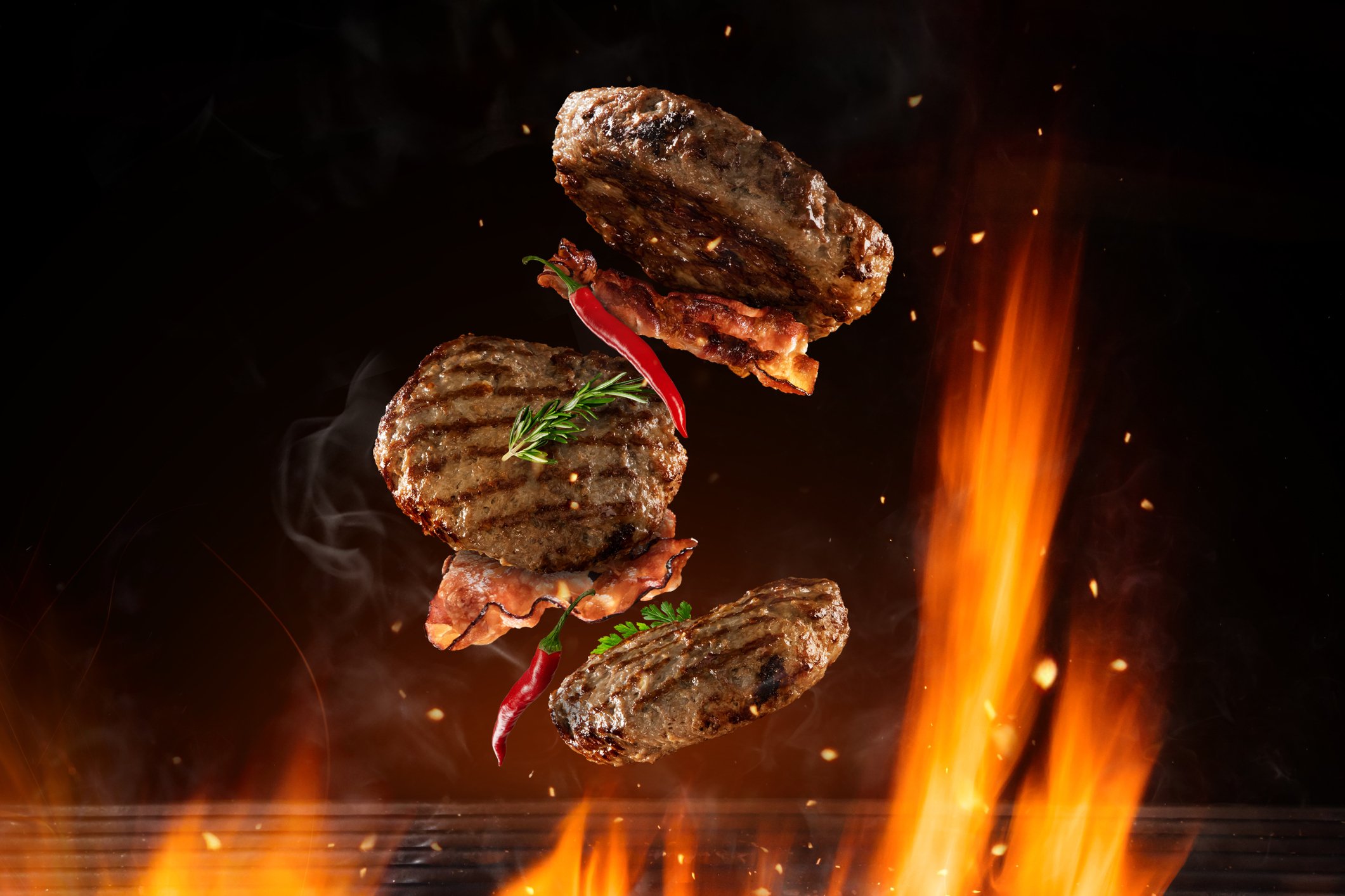 gourmet burgers with peppers flipping above grilling flames