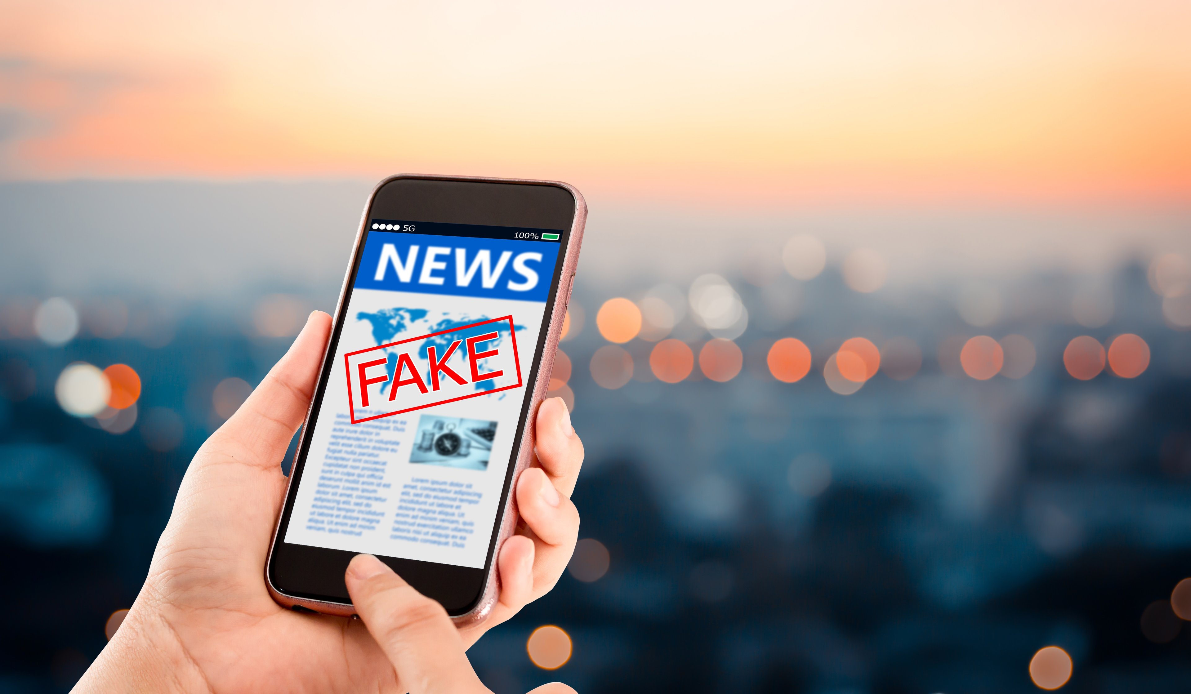 A news story on a smartphone with the word fake in red stamped over it. 