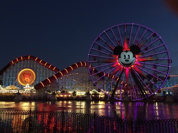Disney California Adventure's Incredicoaster and Mickey Mouse Ferris Wheel lit up at night.