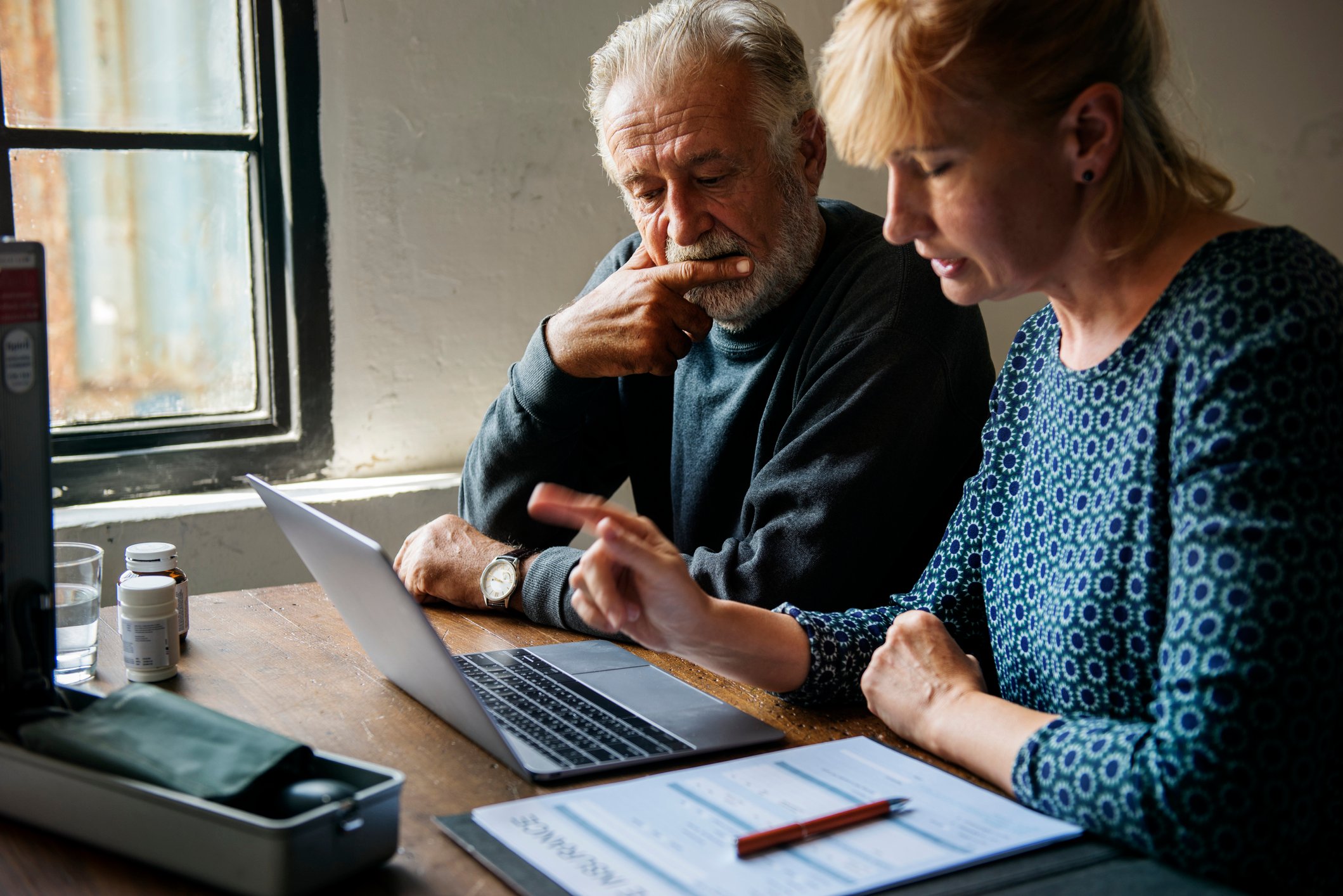An elderly couple at a laptop looking concerned.
