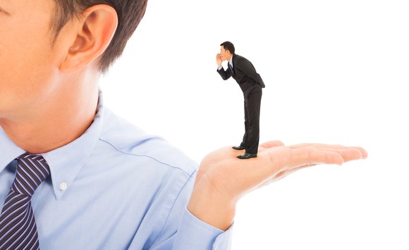 A tiny businessman stands in the palm of a much larger man, saying something in the giant's ear.