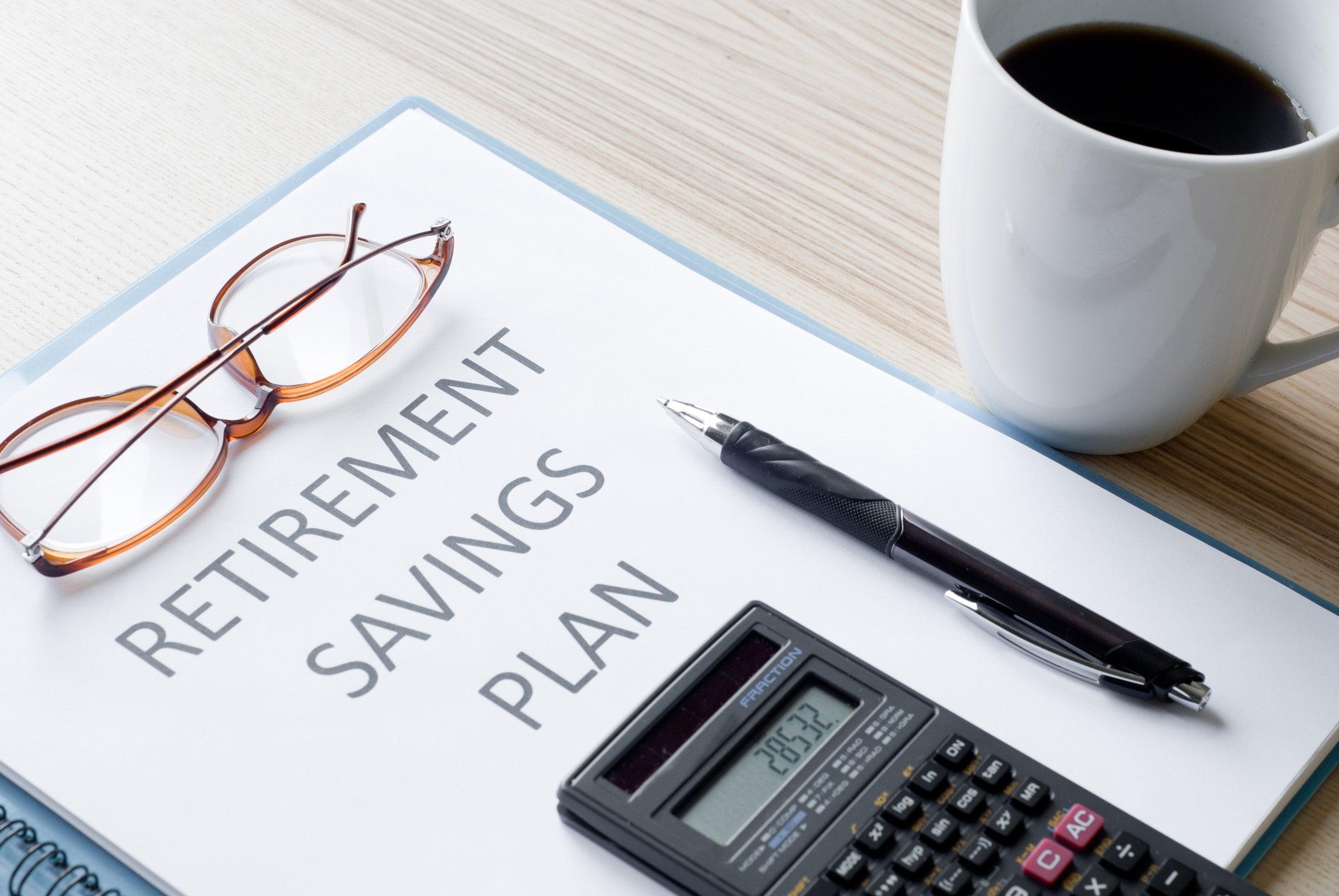 Folder labeled retirement savings plan with calculator, pen, and eyeglasses on it, and mug of coffee next to it
