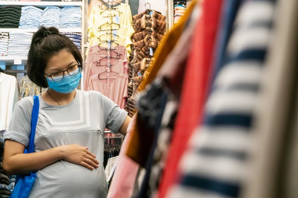 Woman browsing a clothes rack while wearing a medical mask. 